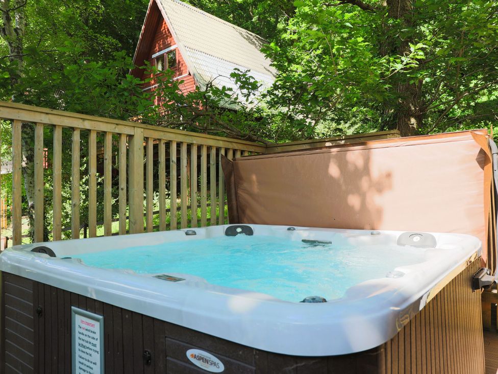 A hot tub on a wooden deck with trees and a house in the background at Lodge 68 - Fern Gully near Finlakes Holiday Park