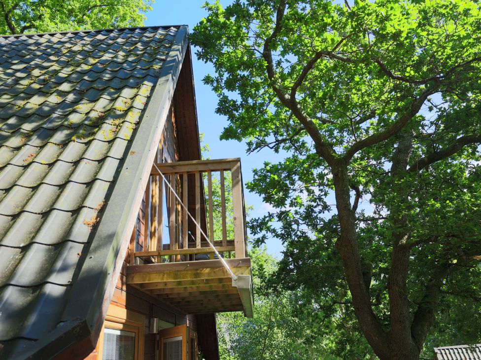 A balcony and roof of a wooden structure surrounded by trees at Lodge 68 - Fern Gully near Finlakes Holiday Park