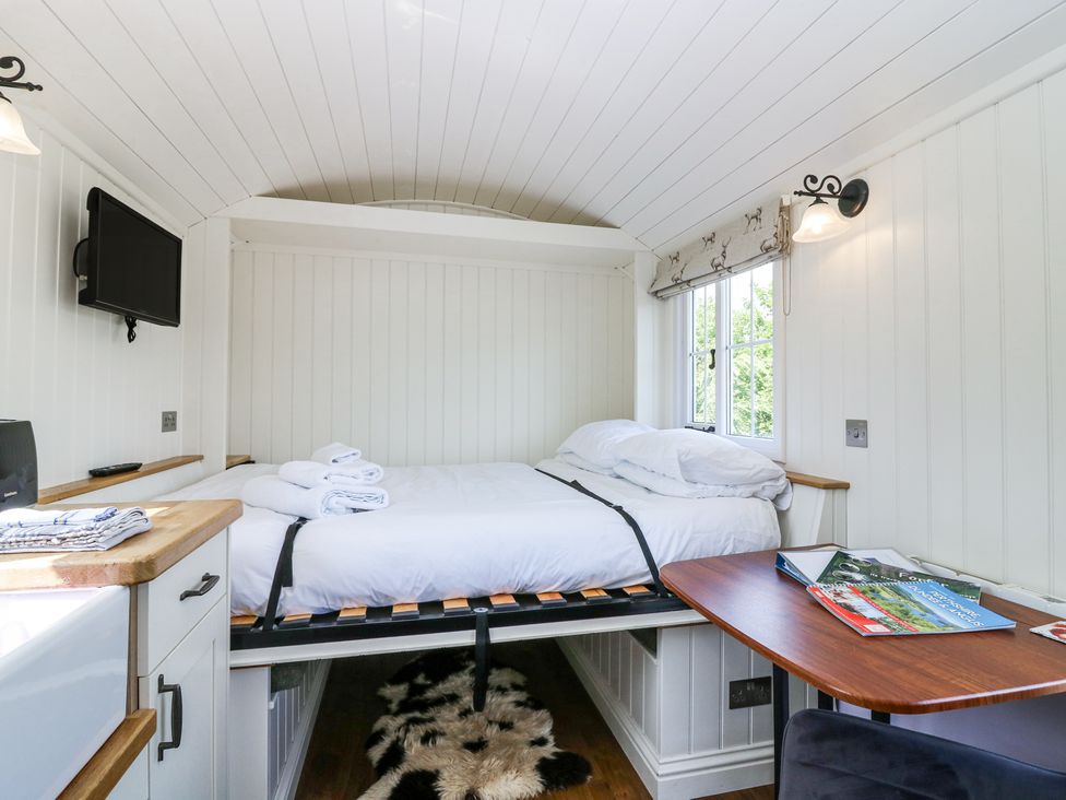 A small bedroom with a bed, a wall-mounted TV, a wooden table with magazines, and a window with a Roman blind at Airlie Burnside near Forfar