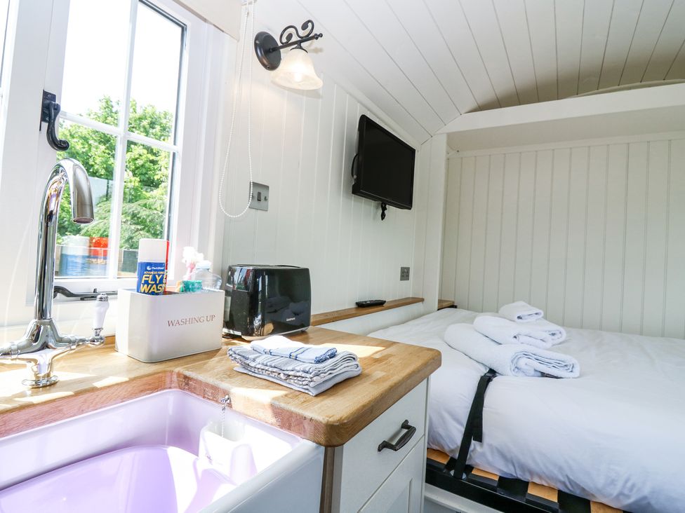 A small kitchen area with a sink toaster and cloths next to a bed with towels and a wall mounted tv at Airlie Burnside near Forfar