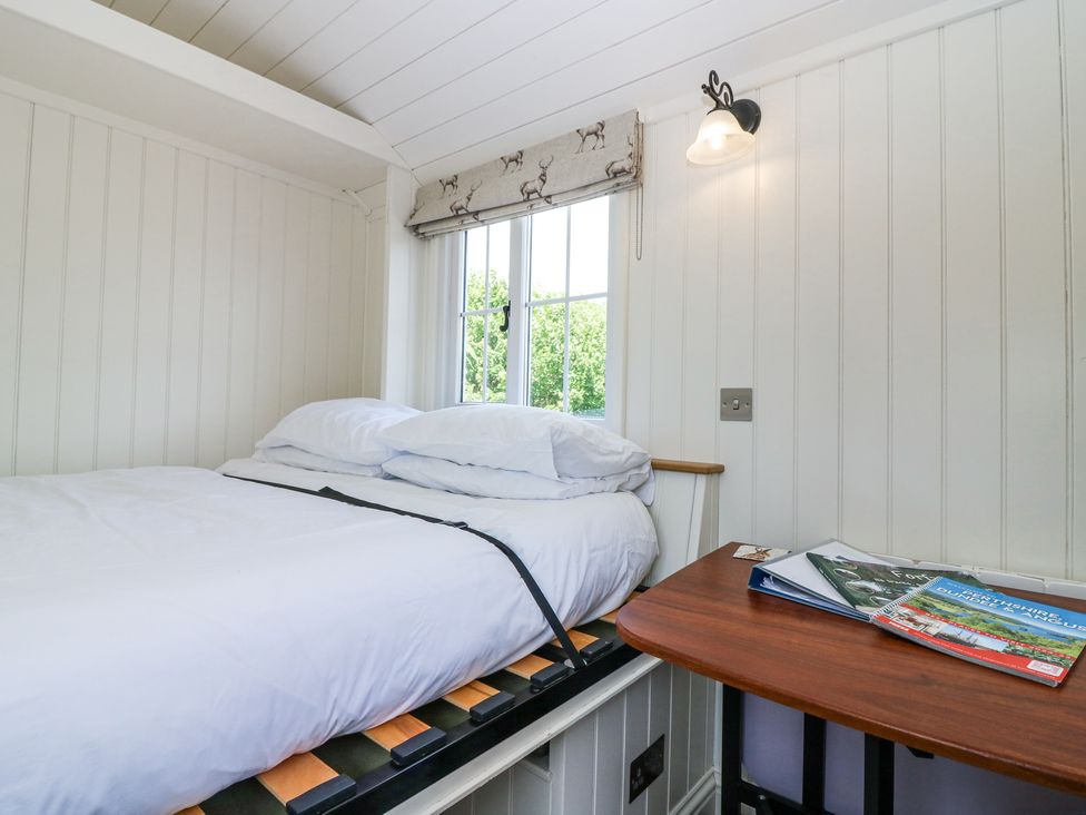A small bedroom with a white bed and pillows next to a window with deer patterned blind and a wooden table with magazines at Airlie Burnside near Forfar