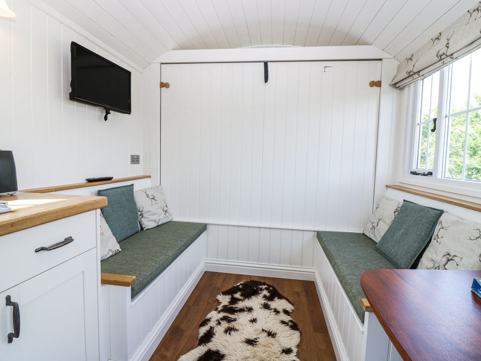 A small room with two green cushioned benches, white paneled walls, a mounted TV, and a window with patterned blinds at Airlie Burnside near Forfar