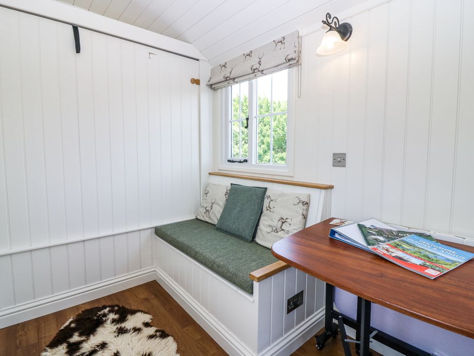 A corner seating area with green cushions next to a window and a wooden table with brochures at Airlie Burnside near Forfar