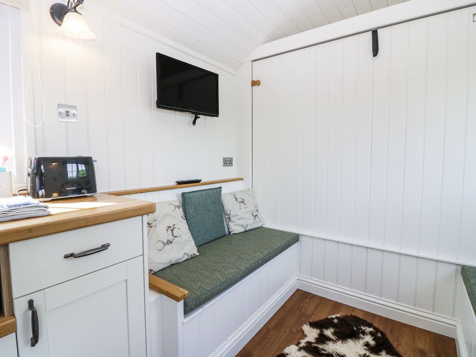 A small seating area with green cushions under a wall-mounted television and a countertop with a toaster at Airlie Burnside near Forfar