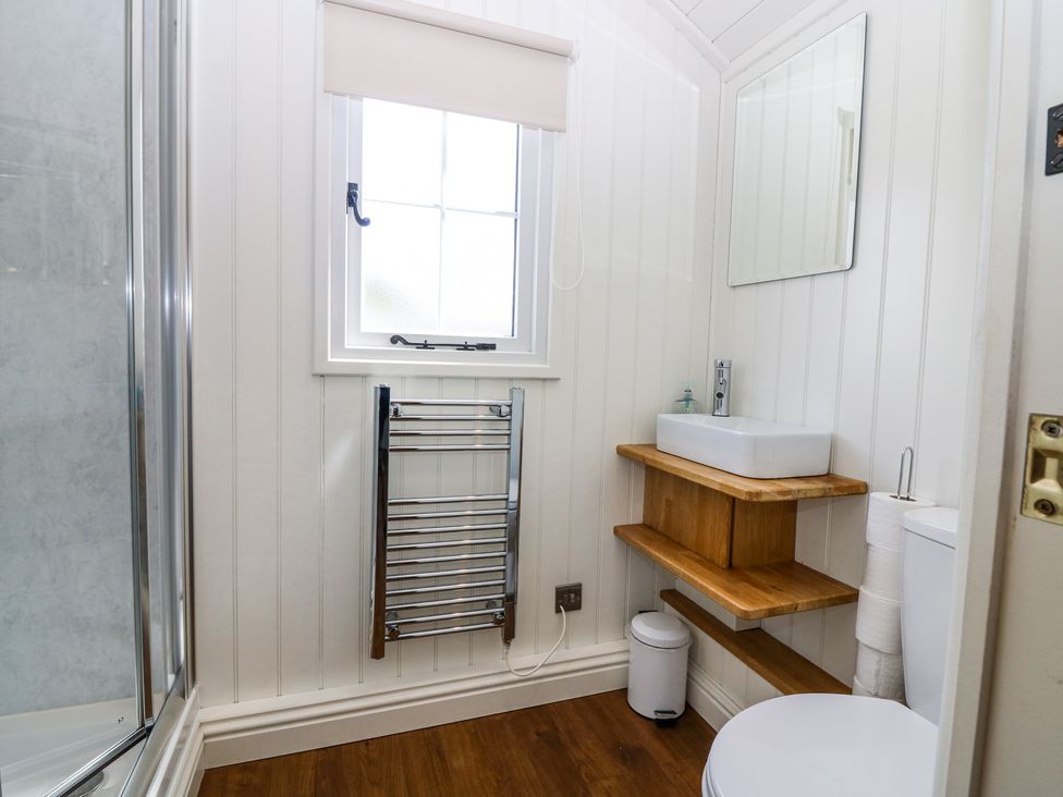 A bathroom with a shower, window, heated towel rail, sink, mirror, toilet, and wooden floor at Airlie Burnside near Forfar