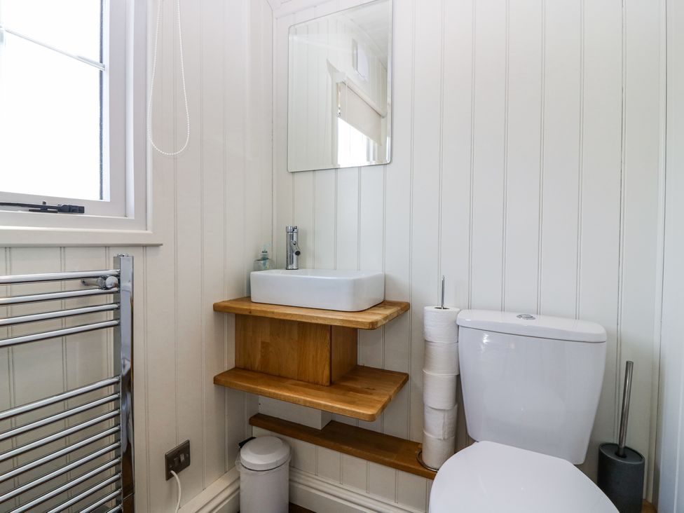 A bathroom with a white toilet and a wooden shelf with a white sink and mirror at Airlie Burnside near Forfar