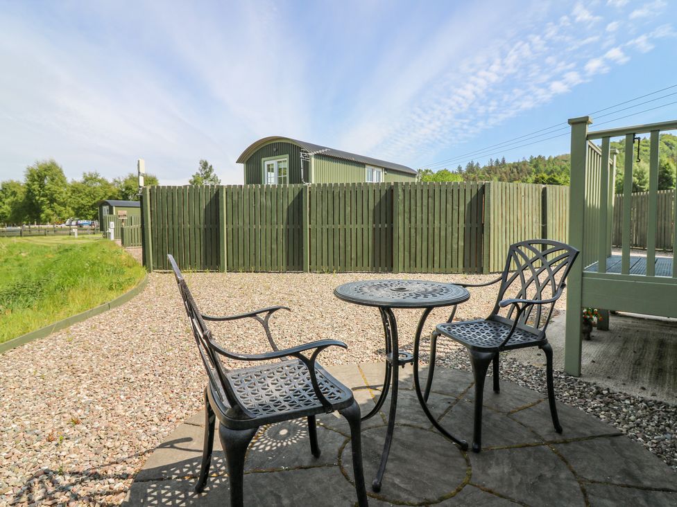 An outdoor patio with a metal table and two chairs on a circular stone platform surrounded by gravel and a green wooden fence at Airlie Burnside near Forfar