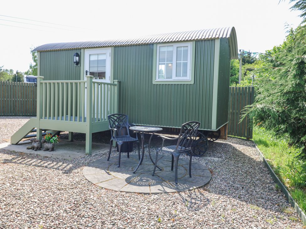 An outdoor seating area with two black metal chairs and a round table on a stone patio next to a green corrugated metal shepherd hut at Airlie Burnside near Forfar