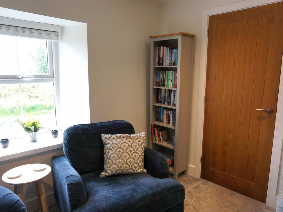 A snug with a chair, bookshelf, and side table at Glendale Trelights near Port Isaac