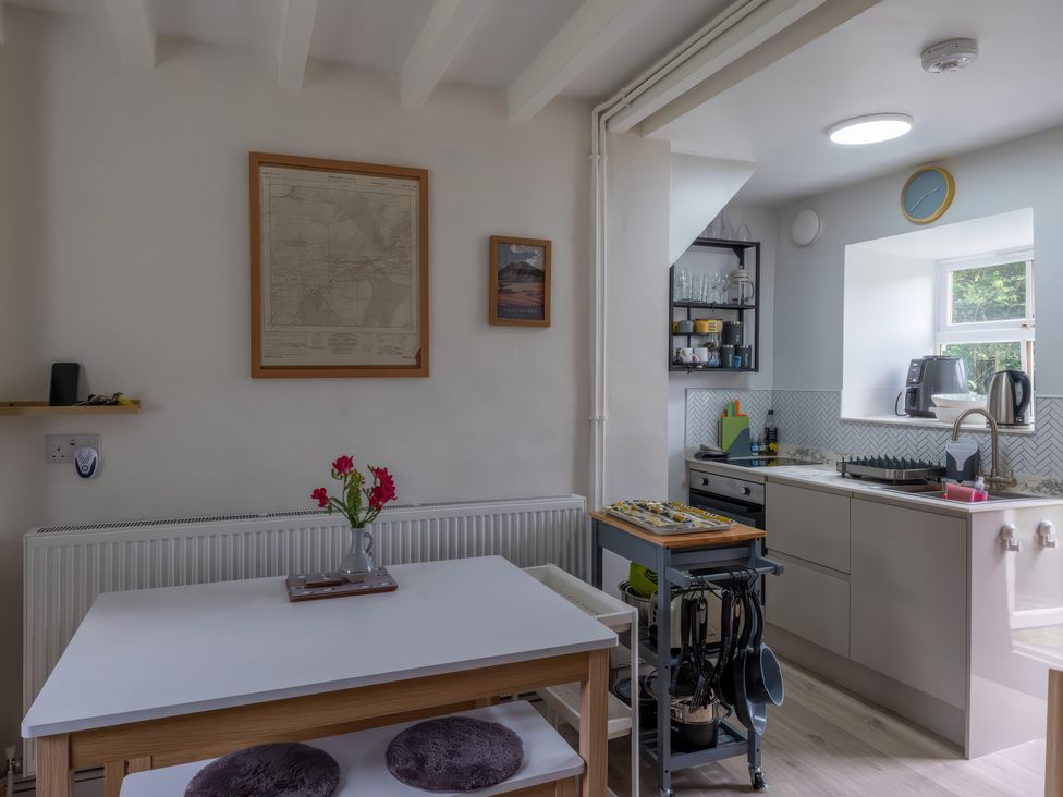 A kitchen with a table and chairs alongside cooking appliances at 1 Aberbeinw Dolwyddelan