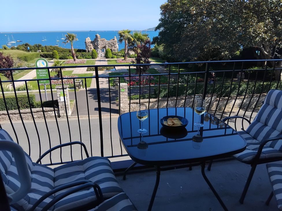A balcony with a table and chairs overlooking a garden and sea at The View in Weymouth