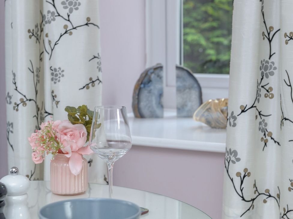 A window with curtains and a table with a flower arrangement and wine glass at The Forge in Morpeth