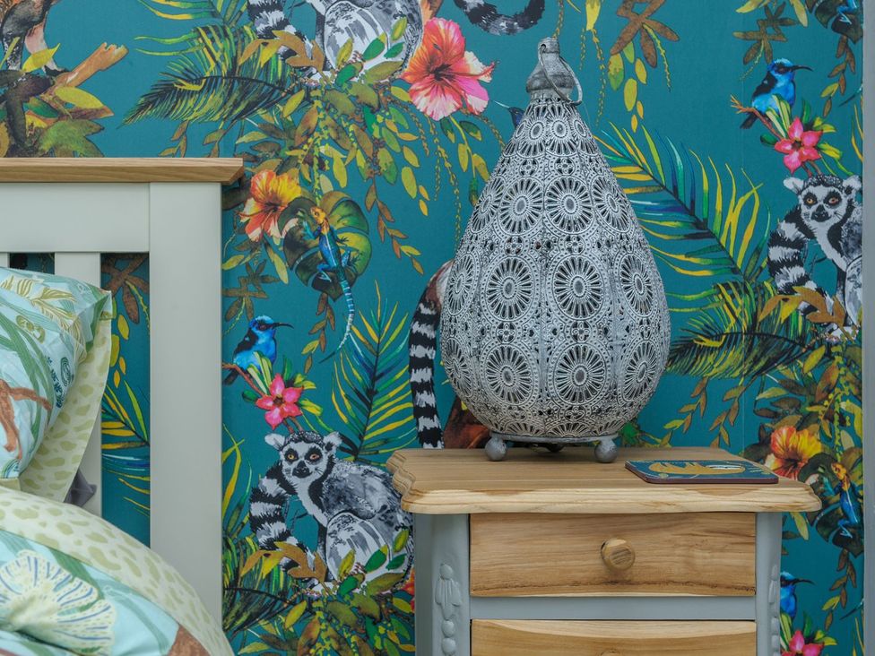 A bedside table with a lamp and patterned wallpaper at The Forge in Morpeth