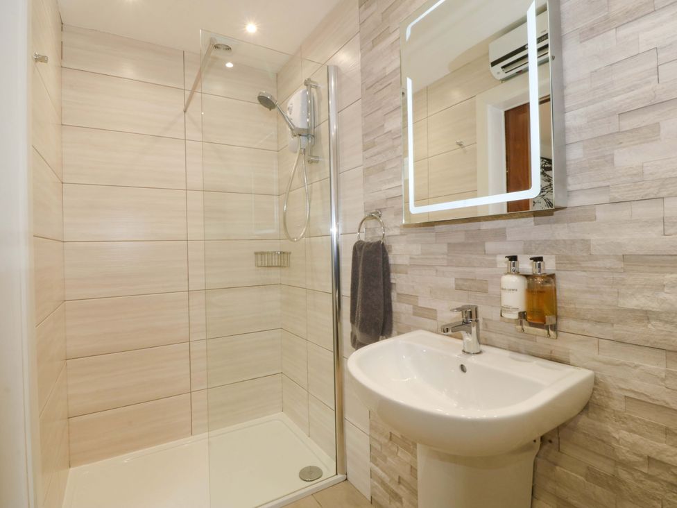 A bathroom with a shower, mirror, and sink at Lodge in Llangefni