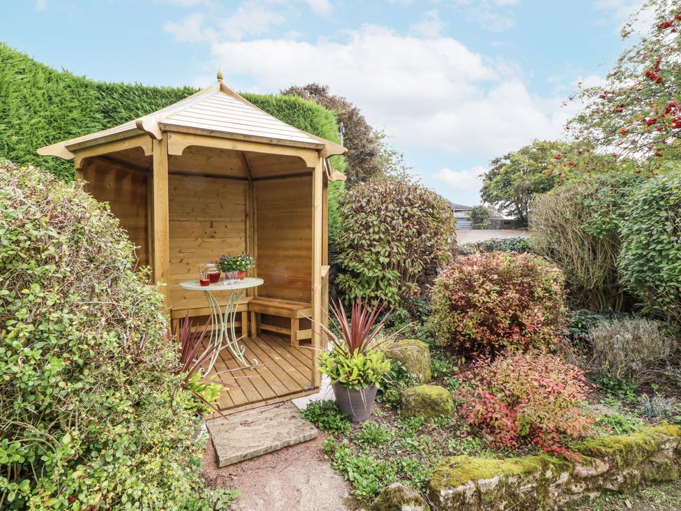 A wooden gazebo with a table and bench in a garden at Peary House in Alnwick