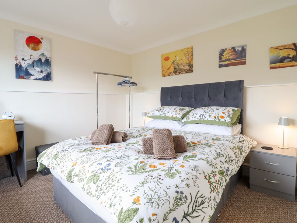 A bedroom with a bed, nightstand, chair, and artwork at Golygfa in Pandy Tudur near Llanrwst
