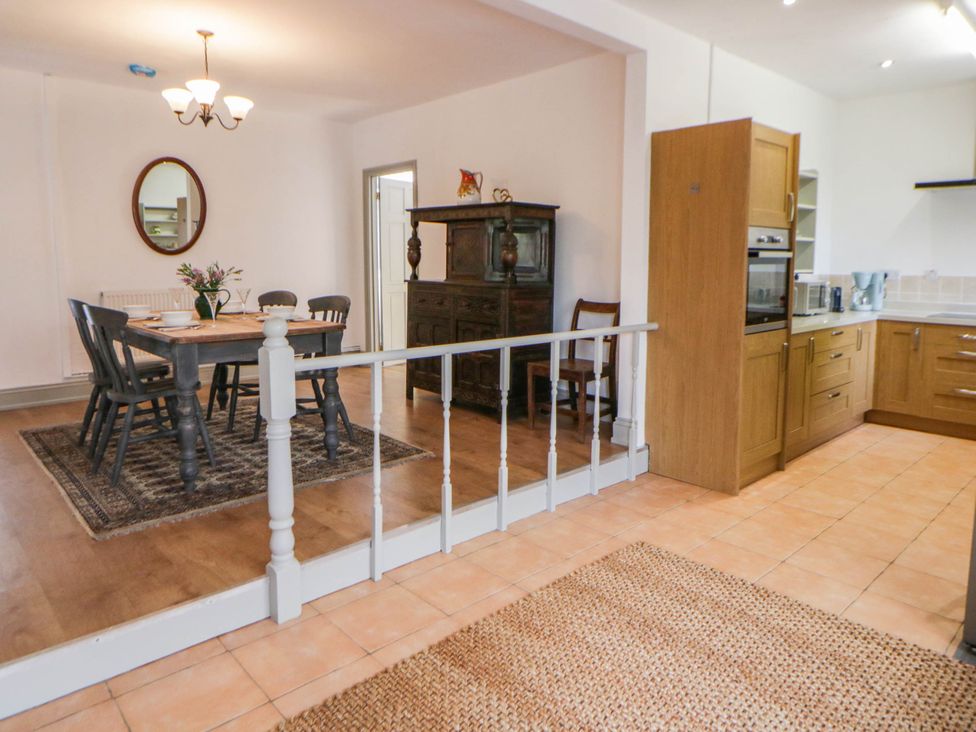 A dining room with a table and chairs leading to a kitchen at Llain in Cardigan