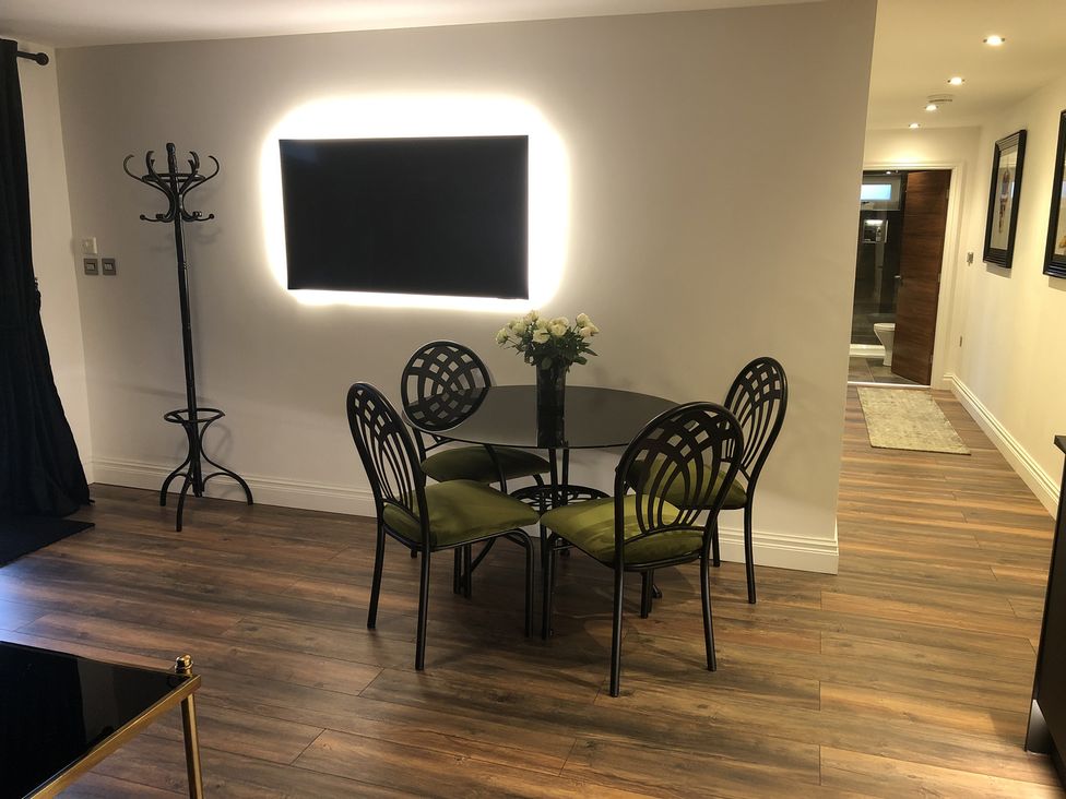 A dining area with a round glass table and four chairs with green cushions at Wayside Lodge in Blackpool