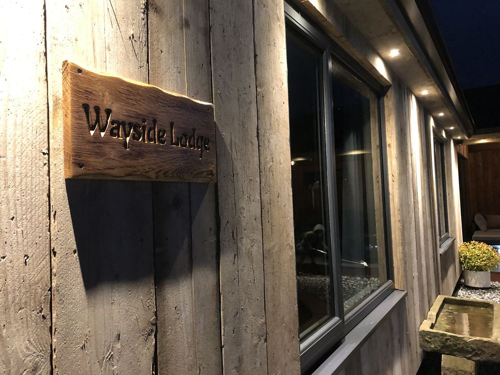 A wooden exterior wall with a Wayside Lodge sign a window and outdoor lighting at Wayside Lodge in Blackpool