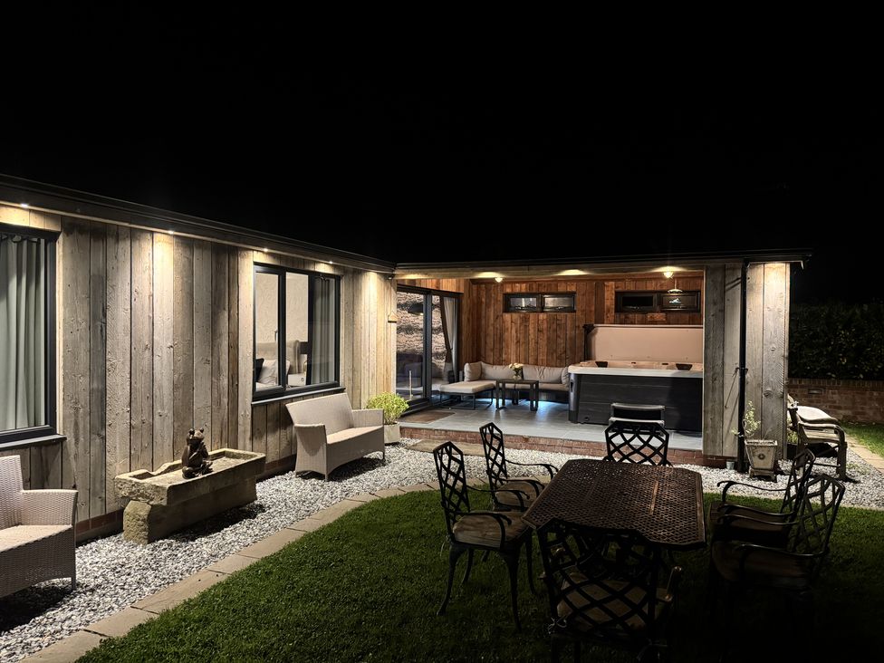 An outdoor patio area at night with wooden walls garden chairs metal table a fountain and a hot tub at Wayside Lodge in Blackpool