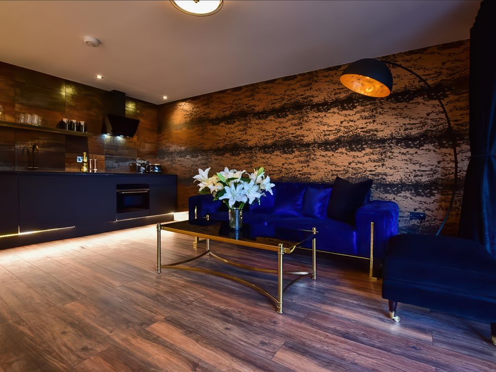 A living area with a blue sofa a gold and black coffee table with white flowers and a kitchen area at Wayside Lodge in Blackpool