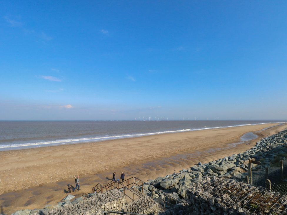 A beach with people walking near the water and wind turbines in the distance at 440 California Sands