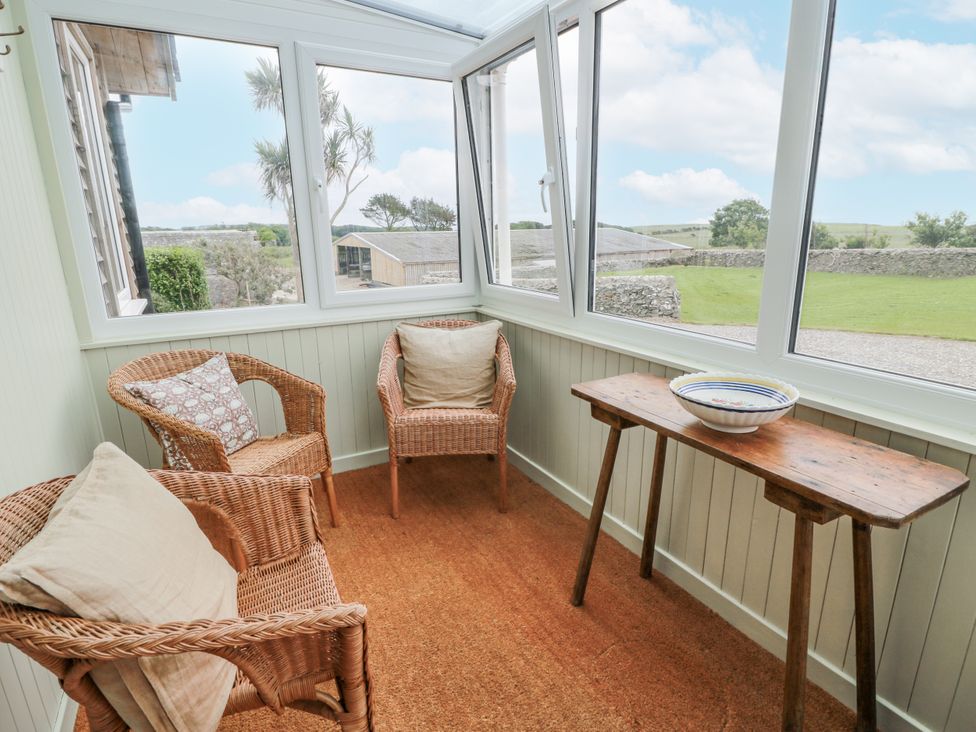 A conservatory with wicker chairs and a wooden table at The Dairy in Newton Stewart