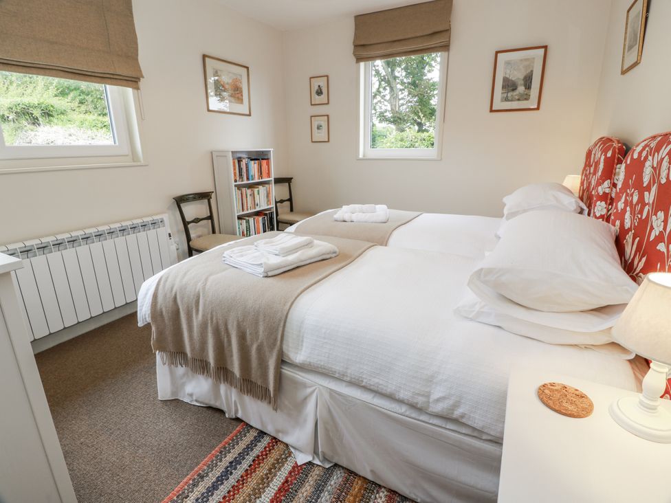A bedroom with two beds, a bookshelf and a lamp at The Dairy in Newton Stewart