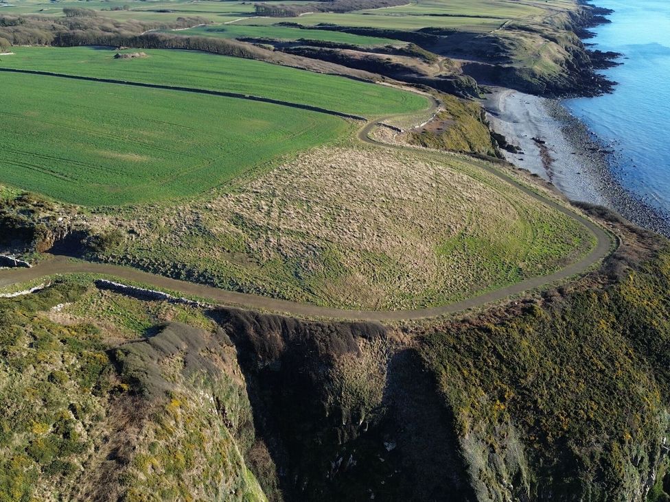 An aerial view of green fields and cliffs by the water at The Dairy in Newton Stewart