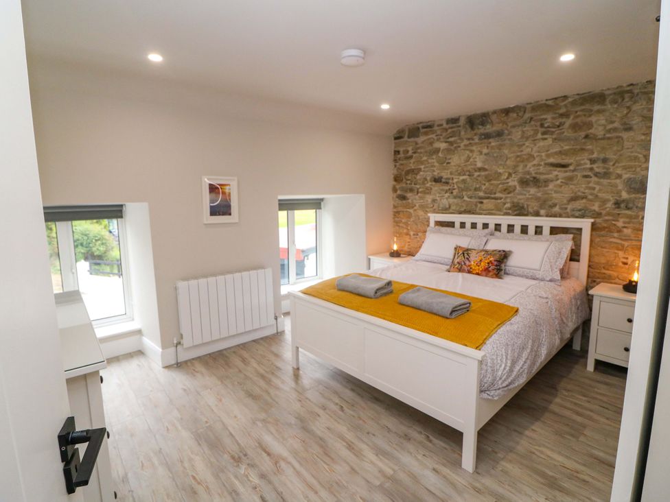 A bedroom with a bed, nightstands, and windows at Valley View House in Kealkill, County Cork