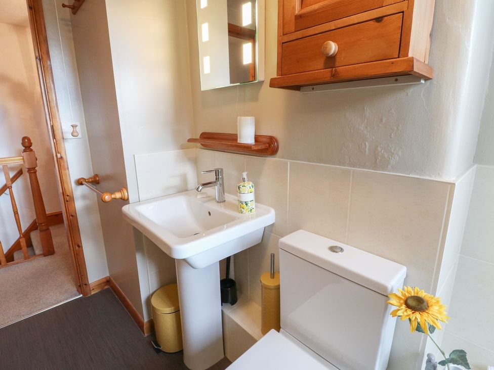 A bathroom with a white sink and toilet a wooden cabinet and a sunflower at The Beehive in Wirksworth