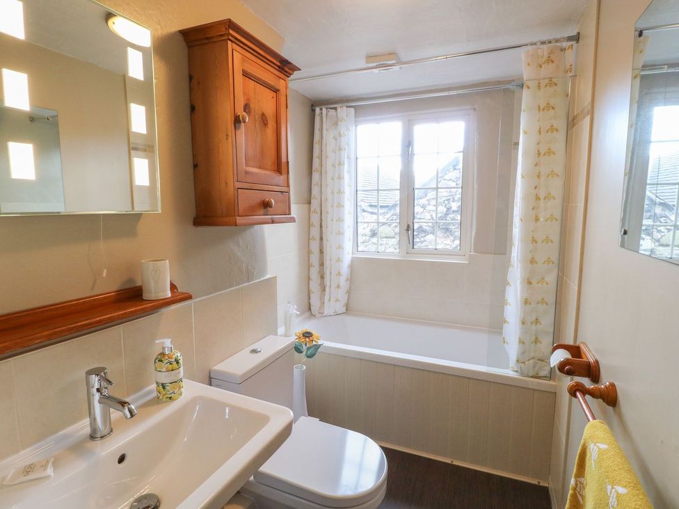 A bathroom with a sink toilet bathtub wooden cabinet and window with bee patterned curtains at The Beehive in Wirksworth