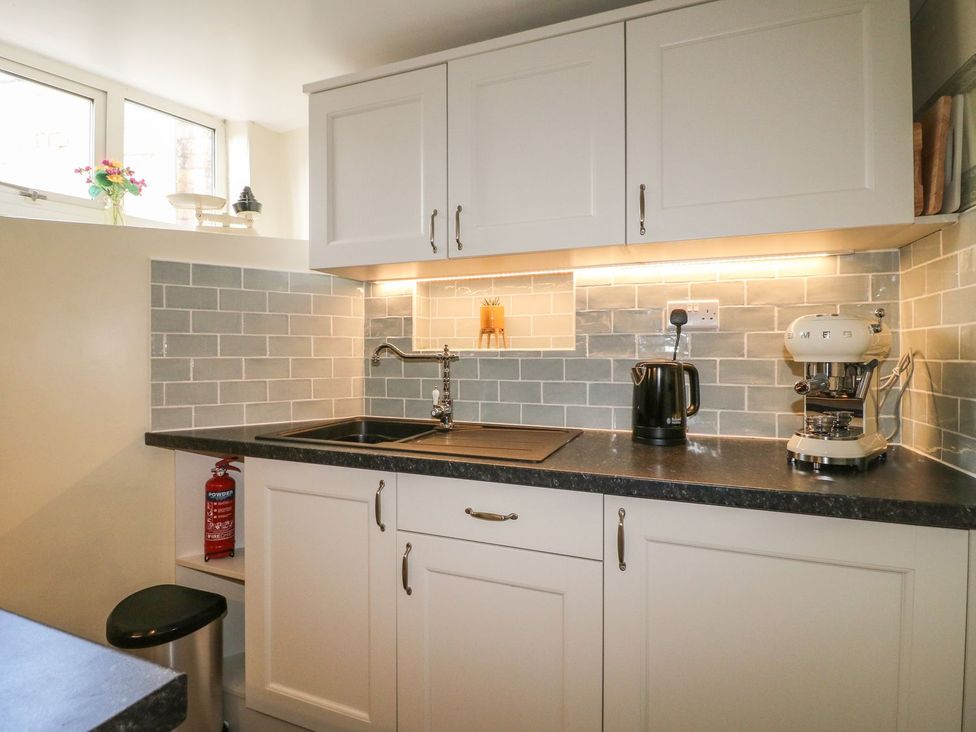 A kitchen with white cabinets a black countertop a sink a kettle and a coffee machine at The Beehive in Wirksworth