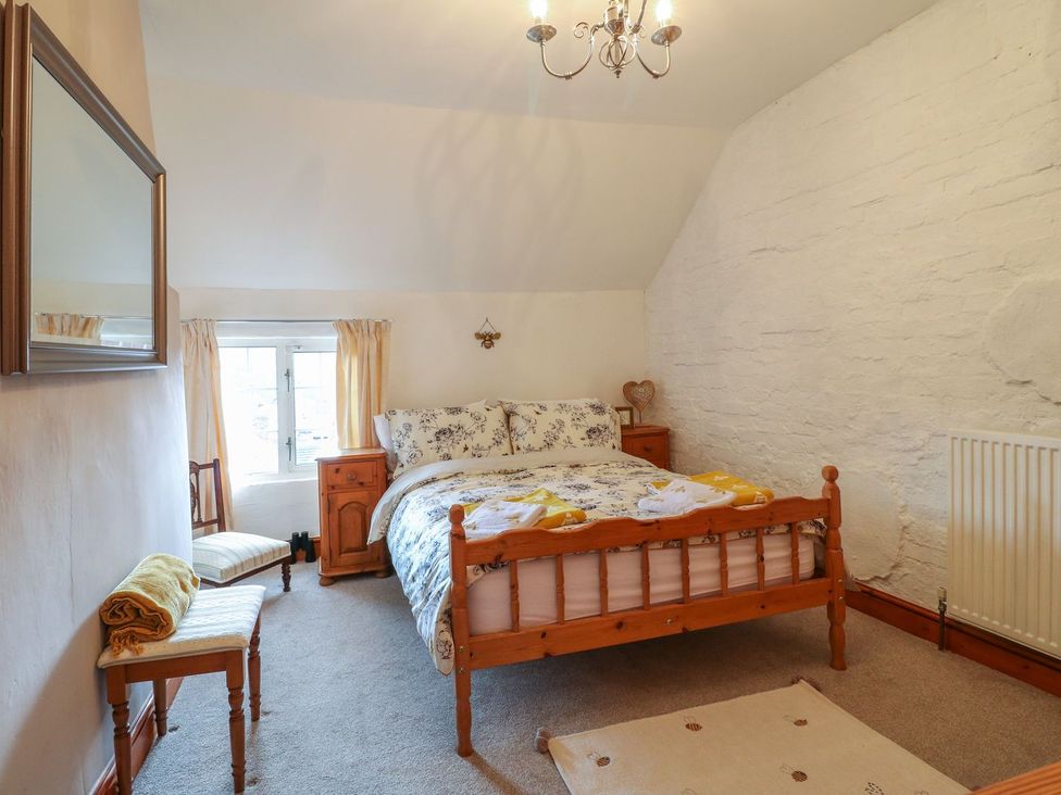 A bedroom with a wooden bed floral bedding two bedside tables and a small window at The Beehive in Wirksworth