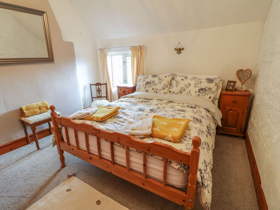 A bedroom with a wooden bed with floral bedding two wooden nightstands a mirror and a window at The Beehive in Wirksworth