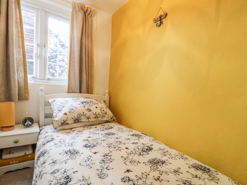 A small bedroom with a single bed and floral bedding next to a window with beige curtains at The Beehive in Wirksworth