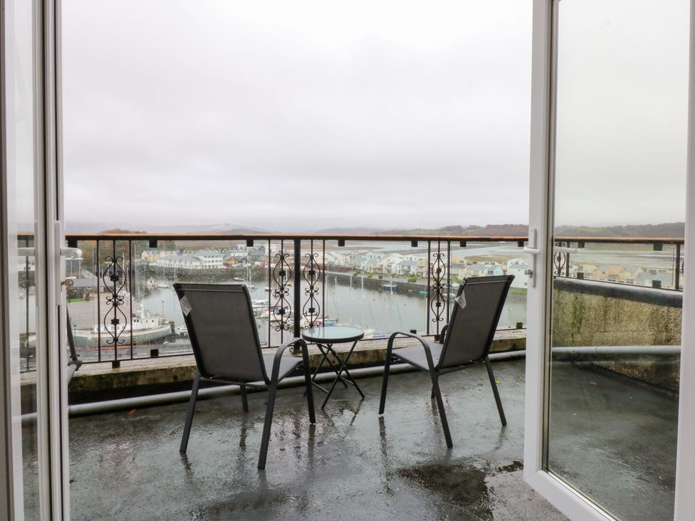 A balcony with chairs and a table overlooking a harbor at Captain’s Quarters in Porthmadog