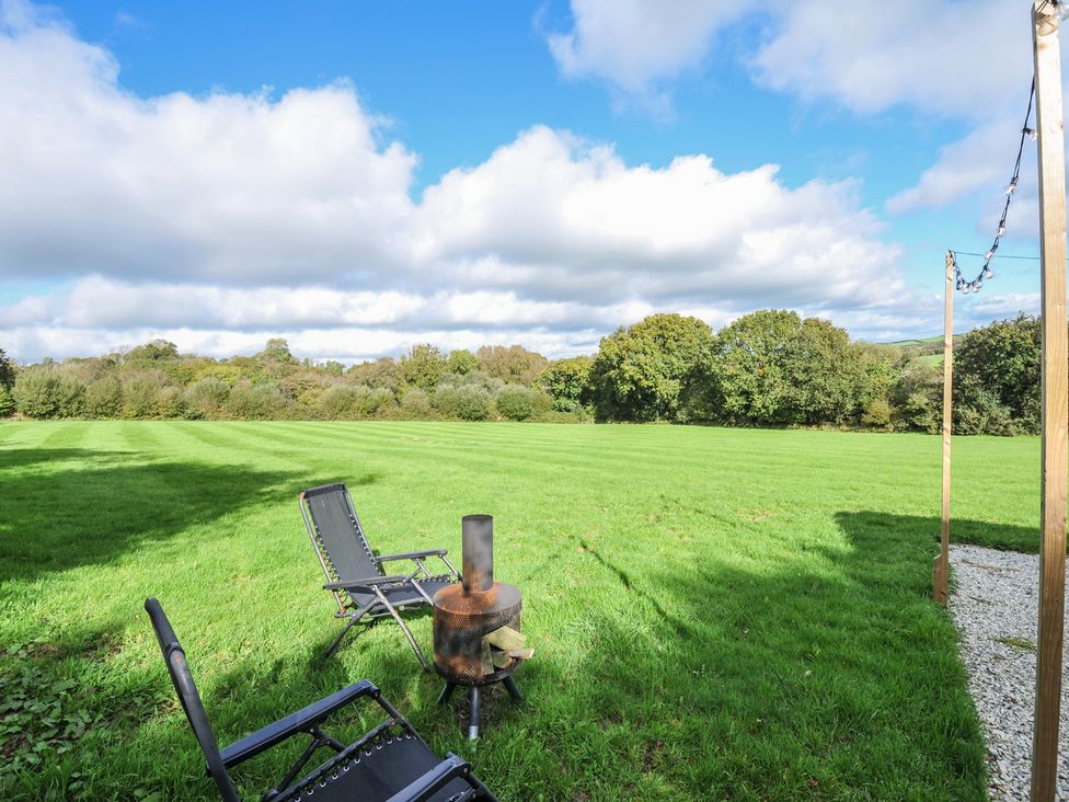 A grassy outdoor area with chairs and a fire pit at Buzzards Lodge in Roche