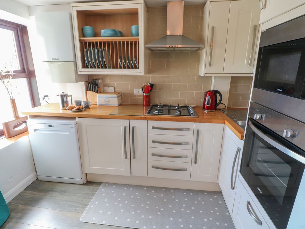 A kitchen with cabinets, a gas hob, a kettle, and a sink at Puffin Nook in Broad Haven