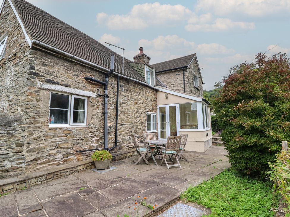 A garden with a stone house and wooden table and chairs at Hafod in Llangollen