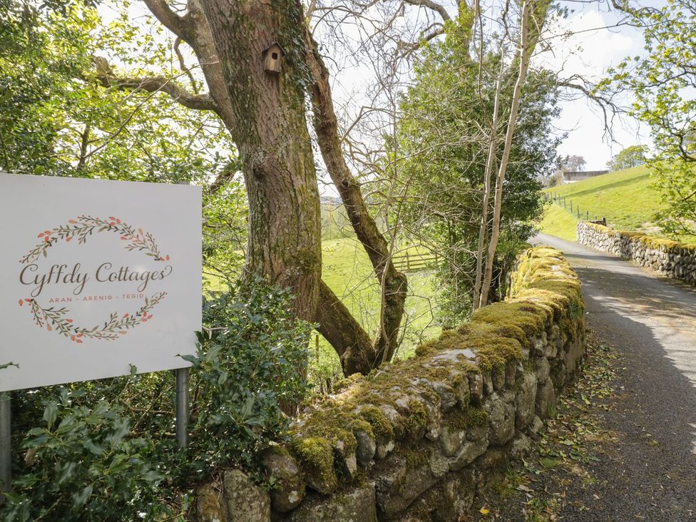 A sign for Cyffdy Cottages next to a tree and a stone wall in Bala