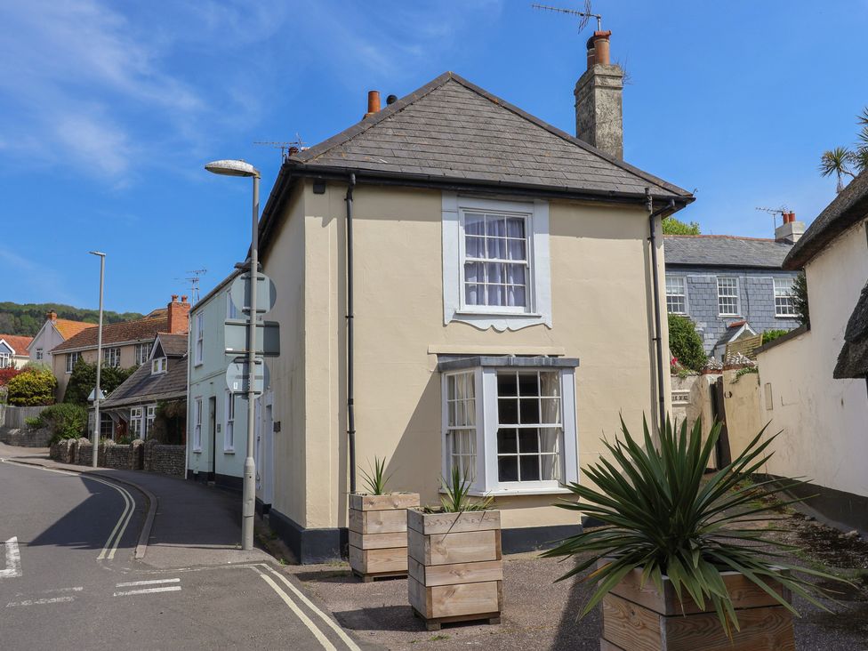 A street view with a cream-colored house and wooden planters with plants at Milton Cottage in Lyme Regis