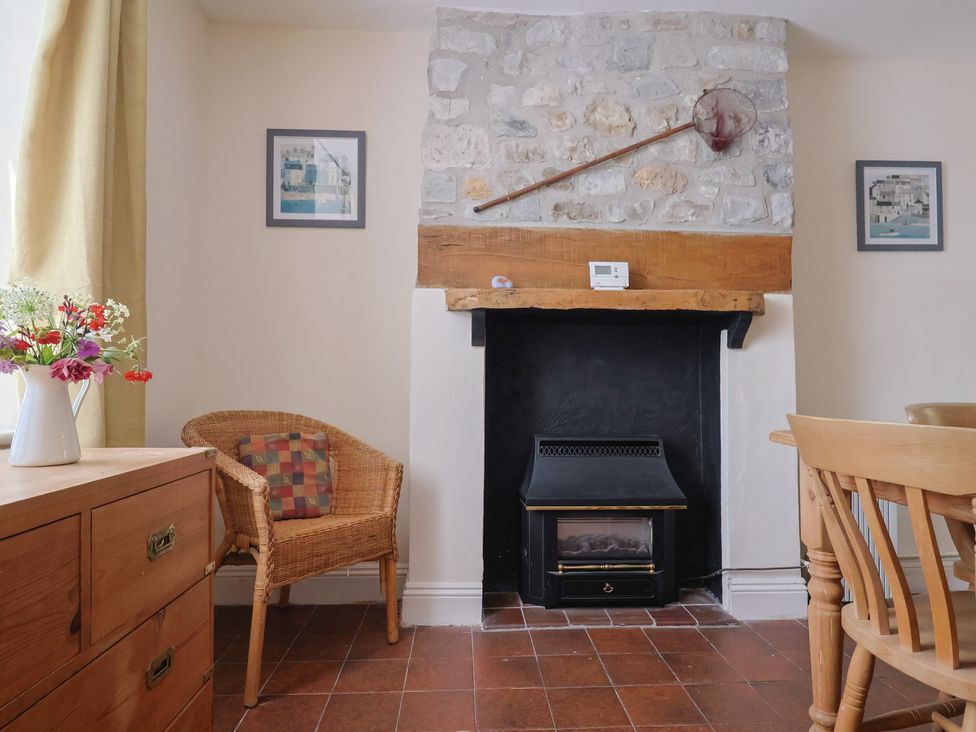 A room with a stone fireplace flanked by two framed pictures a wooden chair wooden drawers and a wooden table with chairs at Milton Cottage Lyme Regis