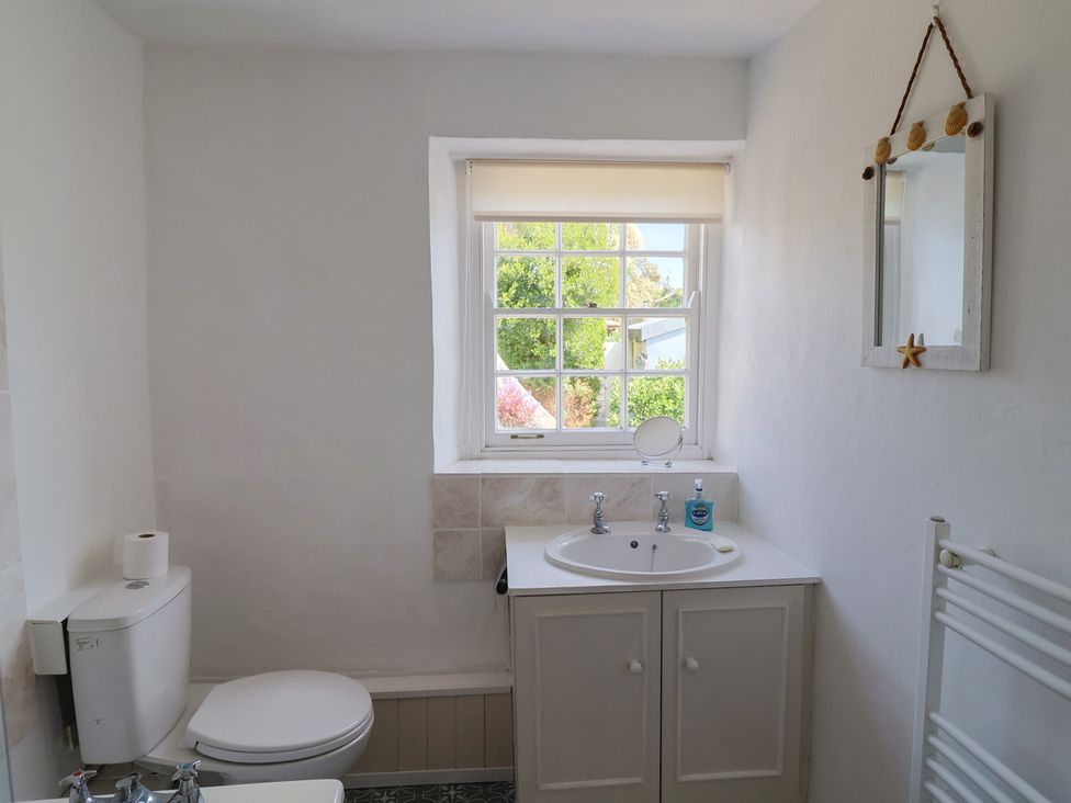 A bathroom with a toilet sink mirror and a window at Milton Cottage in Lyme Regis