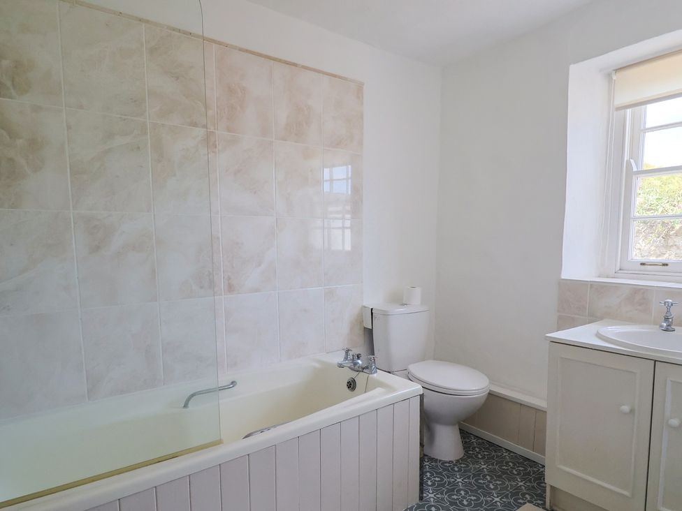A bathroom with bathtub toilet sink cabinet and a window at Milton Cottage in Lyme Regis