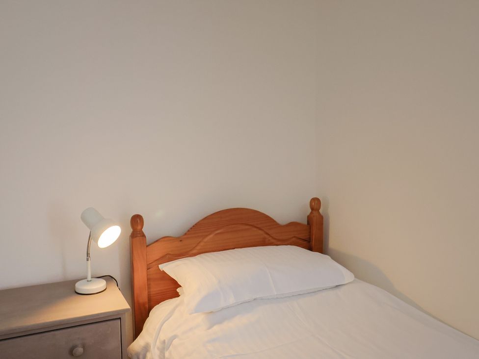 A bedroom with a wooden bed headboard a white pillow white bedding a grey bedside table and a white lamp at Milton Cottage in Lyme Regis