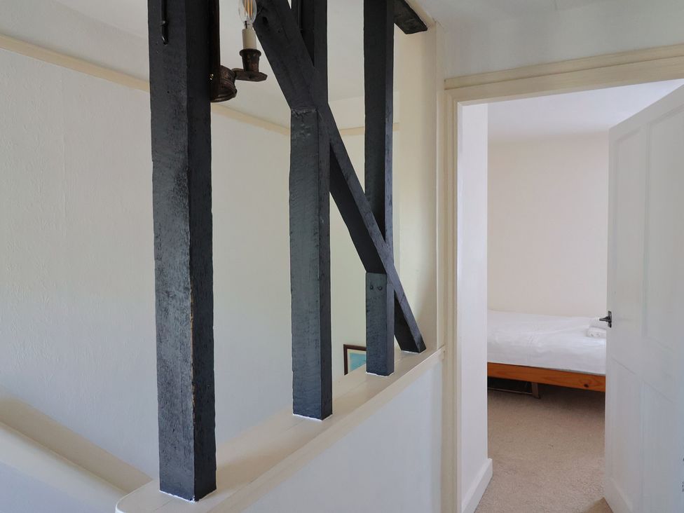 A hallway with black wooden beams and an open door revealing a bedroom with a bed at Milton Cottage in Lyme Regis
