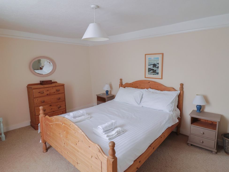 A bedroom with a wooden bed with white linens two bedside tables with lamps a wooden chest of drawers with a mirror above and a framed picture on the wall at Milton Cottage in Lyme Regis