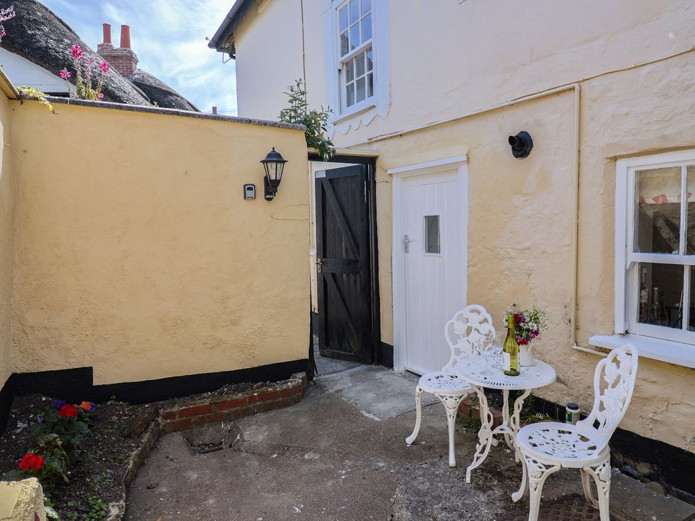 A small courtyard with a white metal table and two chairs and a black wooden gate at Milton Cottage in Lyme Regis
