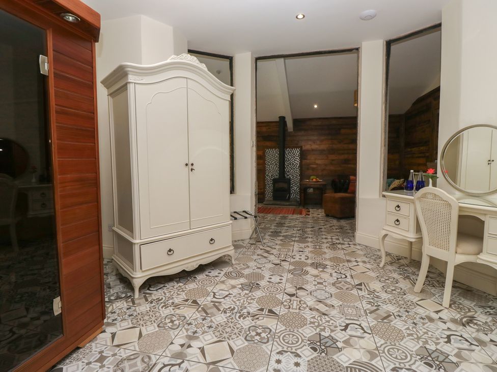 A room with a wardrobe, table, mirror, and stove at Lilac Cottage in Grange-Over-Sands
